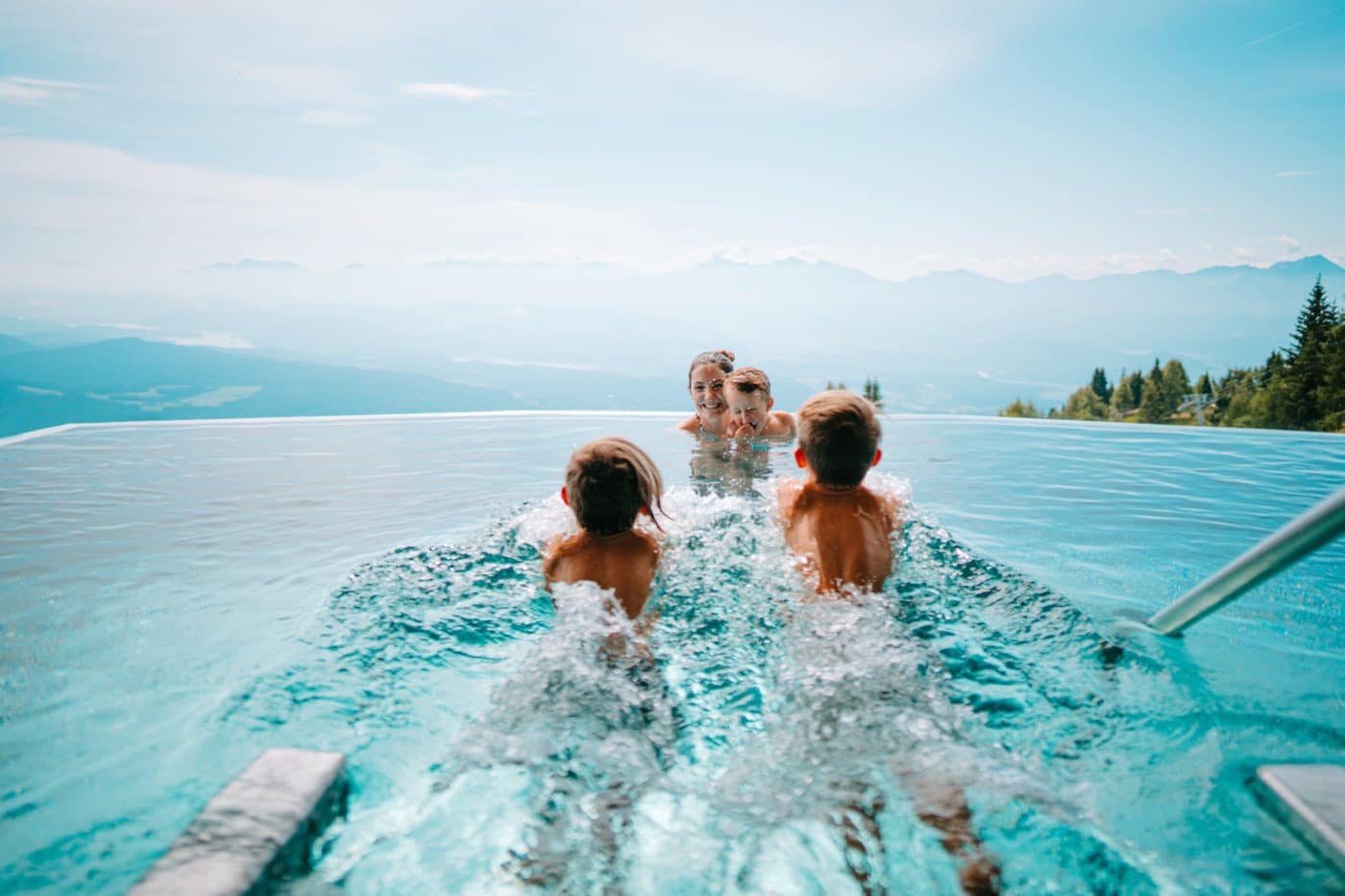 Zwei Kinder planschen im Skypool auf Mutter mit Kleinkind zu, dahinter das Tal