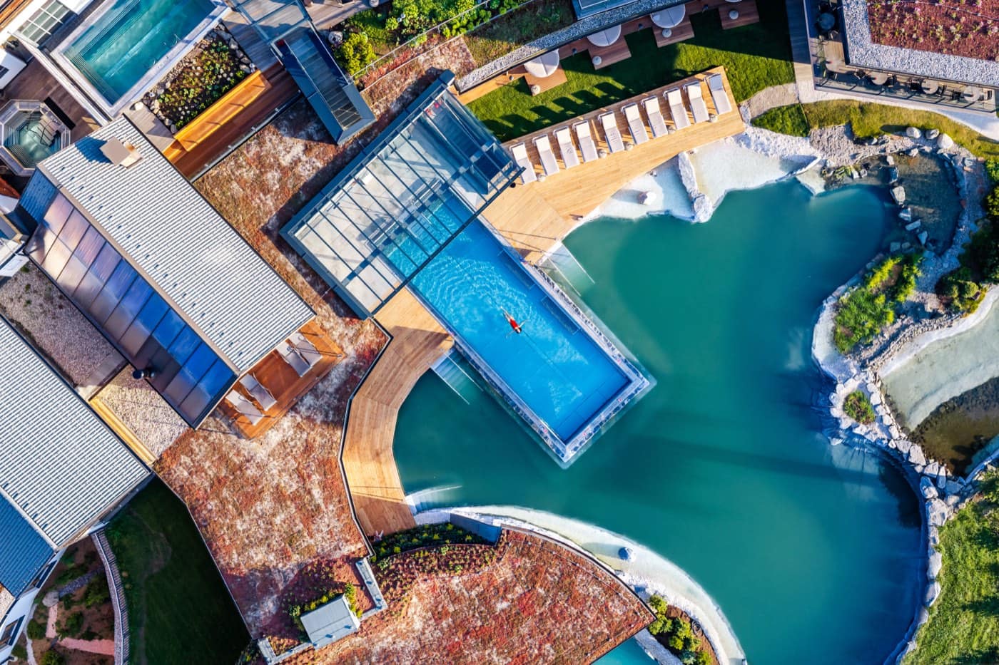 Luftbild senkrecht auf einen Pool mit Glasfront, der über den Naturbadeteich hinausragt