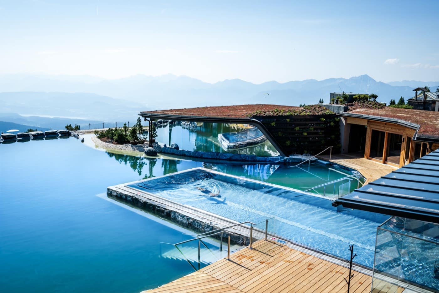 Mehrere ineinandergreifende Pools mit einem Strömungsbecken vor der begrünten Spa-Dachlandschaft