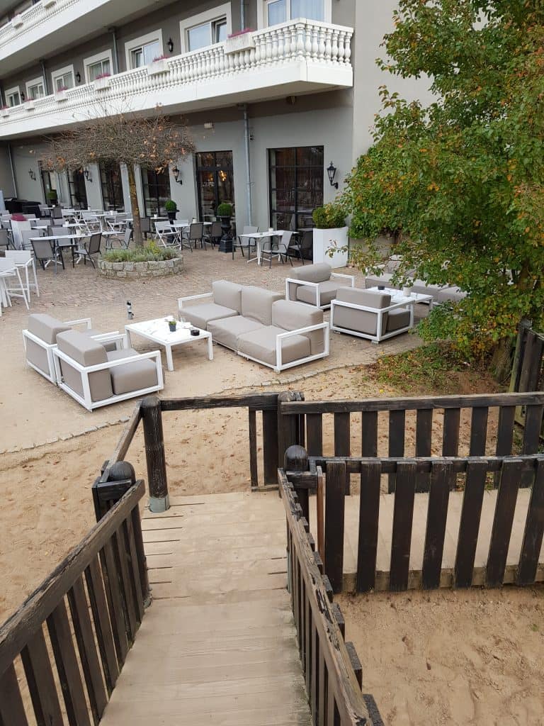 Restaurant-Terrasse mit Lounge-Möbeln, direkt daneben Sand und Holzspielplatz