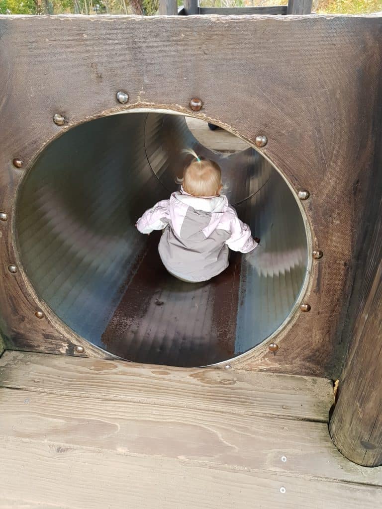 Kleinkind am Eingang der Tunnelrutsche auf dem Holzspielplatz